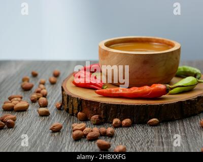 Erdnusssauce in einer kleinen Holzschüssel mit Cayennepfeffer und verstreuten Erdnüssen. Stockfoto