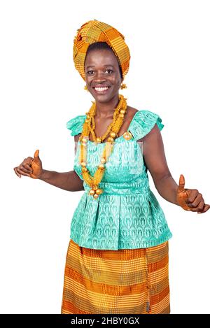 Eine schöne junge afrikanische Frau in traditioneller Kleidung, die auf weißem Hintergrund tanzt und die Kamera lächelnd beobachtet. Stockfoto