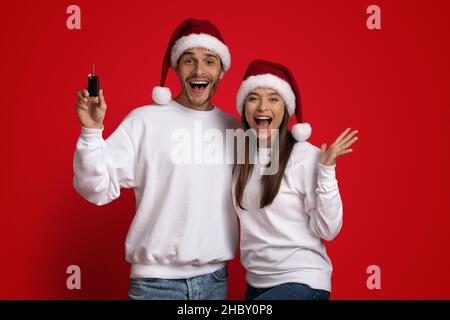 Fröhliches Paar In Santa Hats Hält Den Autoschlüssel Und Ruft Mit Aufregung Aus Stockfoto