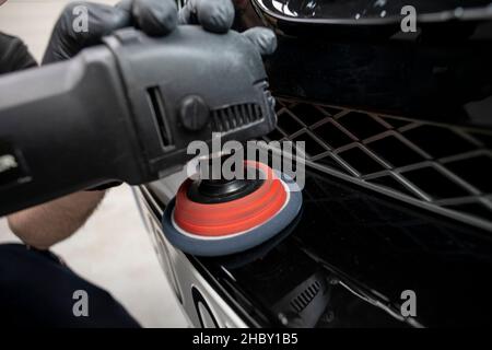 Hand mit einem Polierwerkzeug, um einen Stoßfänger auf einem schwarzen Auto zu reinigen, Nahaufnahme, Detail Stockfoto