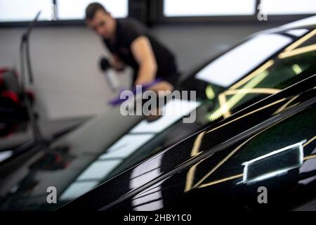 Verschwommener kaukasischer Mann, der die Windschutzscheibe eines Luxuswagens reinigt. Professioneller Arbeiter, in einer Garage. Stockfoto