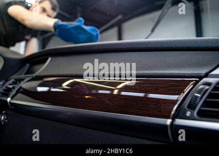 Verschwommener kaukasischer Mann, der die Windschutzscheibe aus dem Inneren eines Luxuswagens putzt. Professioneller Arbeiter, in einer Garage. Stockfoto