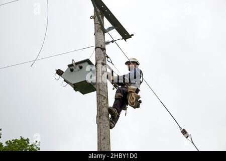 Linienarbeiter, der den alten Strommast ersetzt und Stromkabel auf einem ländlichen Grundstück in Wales, Großbritannien, angeschlossen hat Stockfoto