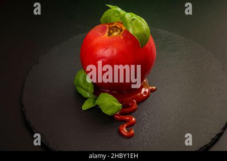Geschälte Tomate mit Ketchup und Basilikumblättern, isoliert auf einer schwarzen Steinfliese Stockfoto