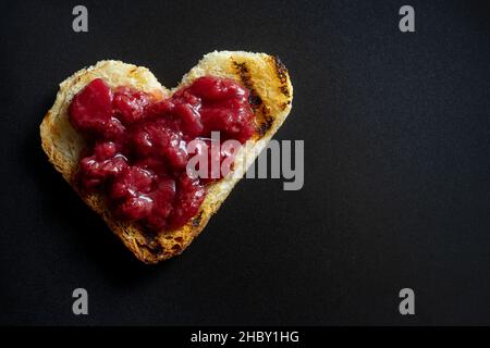 Herzförmiger Toast mit Erdbeermarmelade, isoliert auf Schwarz Stockfoto