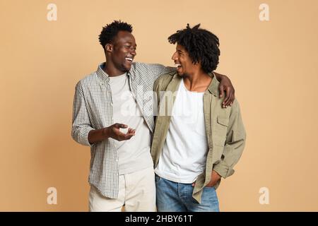 Zwei Fröhliche Schwarze Männliche Freunde Umarmen Und Lachen Auf Beige Hintergrund Stockfoto