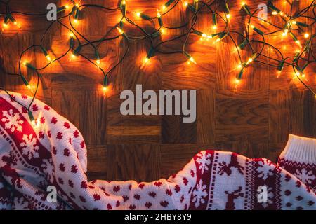 Weihnachtslichter und Strickpullover auf Holzhintergrund. Frohe weihnachten Grußkarte. Flach liegend Stockfoto