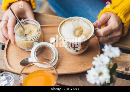 Frau, die Kaffee mit braunem Zucker im Café im Freien getrunken hat. Serviert Cappuccino am Tisch im City Street Restaurant Stockfoto