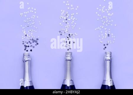 Drei Champagnerflaschen mit Konfetti-Sternen auf fliederfarbenem, sehr perifarbenem Hintergrund. Flat Lay of jubiläum, Bachelorette, Neujahr Feier Konzept Stockfoto
