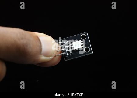 Dreifarbiger SMD-LED-Baustein für programmierbare Mikrocontroller-Platinen, in der Hand gehalten, isoliert auf schwarzem Hintergrund Stockfoto