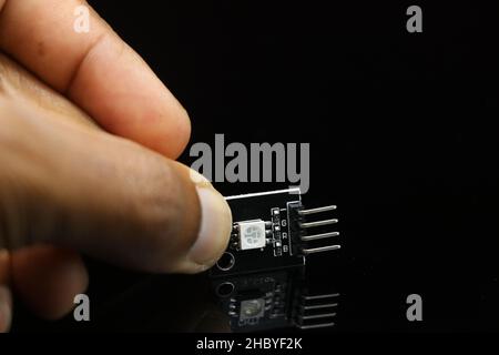 SMD-LED-Modul für programmierbare Micro-Controller-Platinen-Projekte auf reflektierendem schwarzem Hintergrund in der Hand gehalten Stockfoto