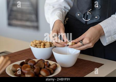 Frauenhände schälen Erdnüsse über einer Schüssel in der Küche, horizontale Nahaufnahme Stockfoto