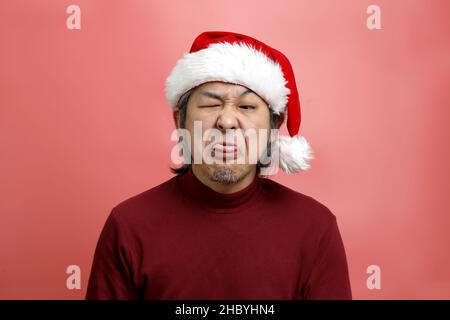 Das asiatische Männerportrait mit weihnachtsmannhut auf dem rosa Hintergrund. Stockfoto