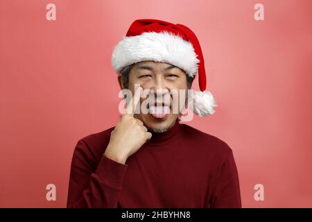 Das asiatische Männerportrait mit weihnachtsmannhut auf dem rosa Hintergrund. Stockfoto