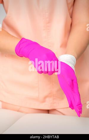 Die Hand der Kosmetikerin legt sterile rosa Handschuhe an und bereitet sich darauf vor, die Kunden im Haus zu empfangen Stockfoto