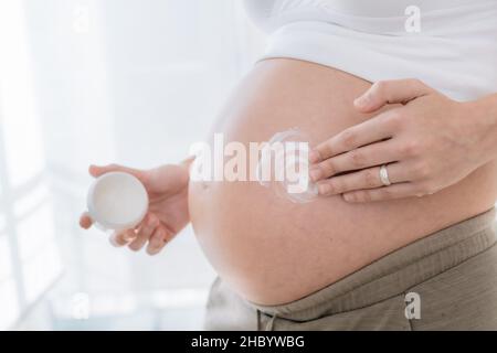 Die Hand der Schwangeren Anwendung feuchtigkeitsspendende Creme auf die Haut ihres Bauches, um Schwangerschaft Dehnungsstreifen zu verhindern. Konzept Gesundheitsversorgung in der Schwangerschaft und sk Stockfoto