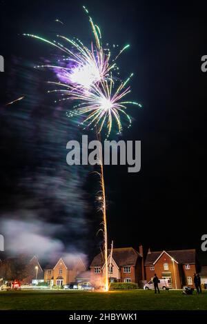 Feuerwerk auf Dorfgrün mit Feuerwerk explodiert auf einer goldenen feurigen Spur in abstraktem, verschwommenem Muster am Himmel über einer Reihe von Häusern. Stockfoto