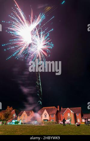 Feuerwerk auf Dorfgrün mit Feuerwerk explodiert auf einer goldenen feurigen Spur in abstraktem, verschwommenem Muster am Himmel über einer Reihe von Häusern. Stockfoto