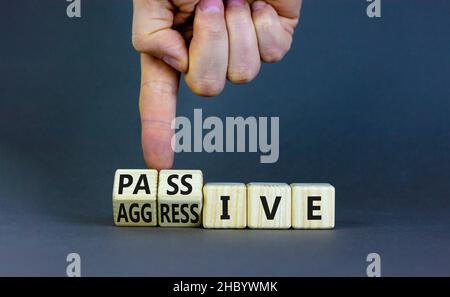 Passives oder aggressives Symbol. Geschäftsmann dreht Holzwürfel und ändert das Wort passiv in aggressiv. Schöner grauer Hintergrund, Kopierbereich. Bus Stockfoto