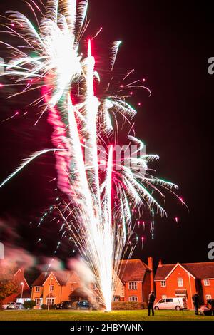 Feuerwerk auf Dorfgrün mit Feuerwerk explodiert auf einer goldenen feurigen Spur in abstraktem, verschwommenem Muster am Himmel über einer Reihe von Häusern. Stockfoto