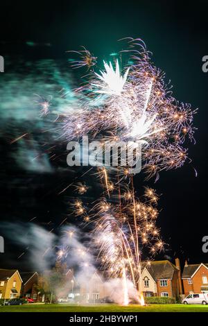 Feuerwerk auf Dorfgrün mit Feuerwerk explodiert auf einer goldenen feurigen Spur in abstraktem, verschwommenem Muster am Himmel über einer Reihe von Häusern. Stockfoto