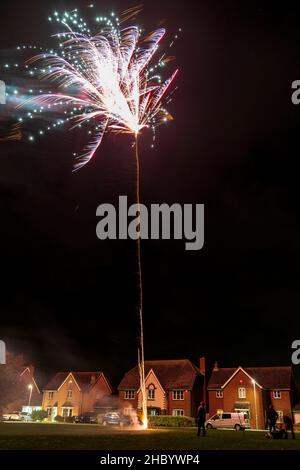 Feuerwerk auf Dorfgrün mit Feuerwerk explodiert auf einer goldenen feurigen Spur in abstraktem, verschwommenem Muster am Himmel über einer Reihe von Häusern. Stockfoto
