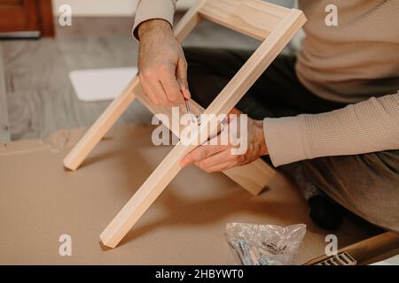 Ein erfahrener Mann montiert zu Hause Holzmöbel mit einem Sechskantschlüssel Stockfoto