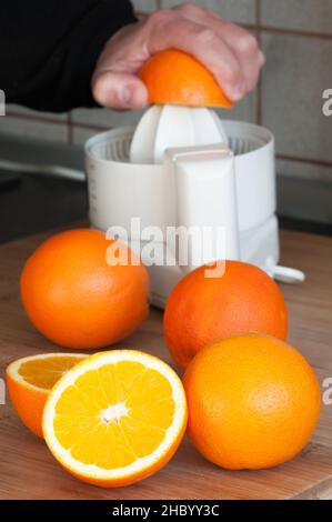 Orangensaft: Nahaufnahme eines in zwei Hälften geschnittenen Orangen mit einem verschwommenen elektrischen Entsafter im Hintergrund Stockfoto