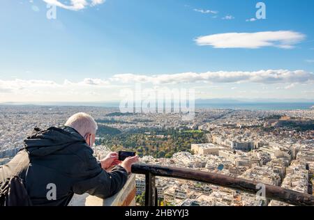 Horizontale Nahaufnahme eines Touristen, der vom höchsten Berg Lycabettus, Griechenland, aus den Blick auf die Akropolis und die Stadt Athen fotografiert. Stockfoto