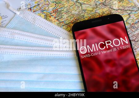 Omicron-Variante. Smartphone mit „Omicron“-Text auf abstrakter Unschärfe-Darstellung von roten Viren mit Schutzmasken und Karten. SARS-CoV-2, B.1.1.529. Schutz Stockfoto