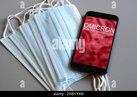 Omicron-Variante. Smartphone mit „Omicron“-Text auf abstrakter Unschärfe-Darstellung von roten Viren mit Schutzmasken und geografischen Karten. SARS-CoV-2, B.1.1.52 Stockfoto