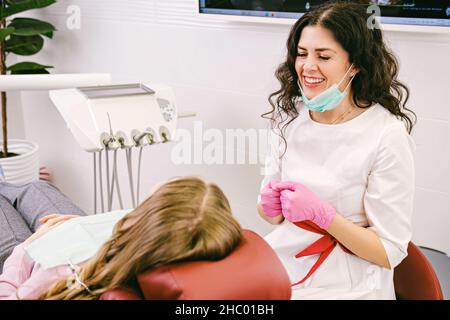 Schöne Zahnarzt junge Frau lächelnd, während das Tragen einer chirurgischen Maske zum Schutz und Handschuhe mit einem Patienten im Schrank. Stockfoto