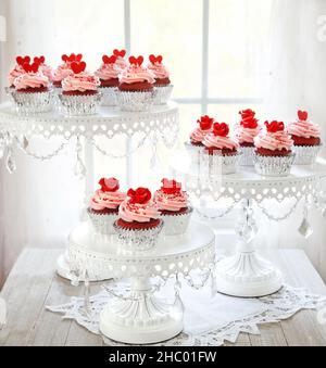 Rote Samt-Cupcakes mit rosa Vanillefrosting, verziert mit roten Rosen auf einem dreistufigen Ständer. Stockfoto