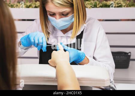 Kosmetologin professionelle Manikuristin Frau in medizinische Maske und schützenden Handschuhen machen Maniküre für einen Kunden auf Pandemie Zeit. Stockfoto