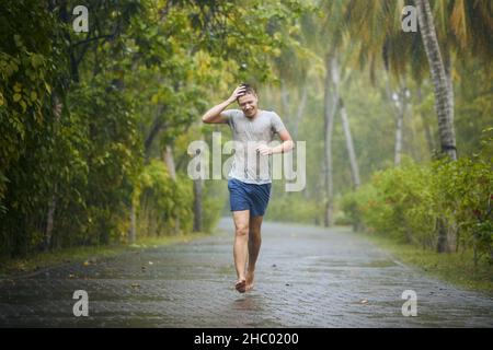 Durchnässt junger Mann, der bei starkem Regen auf der Straße läuft. Stockfoto