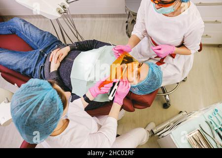 Professioneller Zahnarzt mit einem Assistenten, der ein Stomatologie-Verfahren für einen Mann-Patienten im Zahnarztstuhl macht. Stockfoto