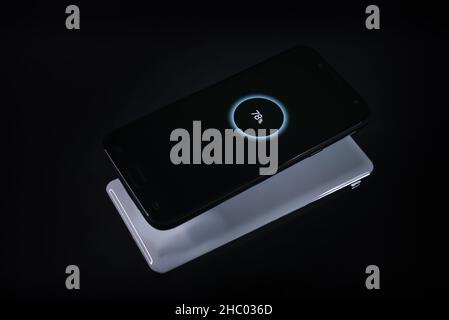 Smartphone während kabelloses Laden von einem Ladegerät auf schwarzem Hintergrund Stockfoto