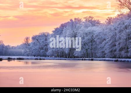 Münsterland, NRW, Deutschland. 22nd Dez 2021. Ein wunderschöner Sonnenuntergang schließt den Tag ab. Das plötzliche kältere Wetter hat eine dicke Schicht anhaltendem Frost auf Bäumen und Wiesen hervorgebracht, die das Münsterland bei Dülmen in ein malerisches Winterwunderland mit herrlichem Sonnenschein verwandelt. Der Kälteeinbruch soll bis morgen fortgesetzt werden, wenn milderes Wetter zurückkehrt. Kredit: Imageplotter/Alamy Live Nachrichten Stockfoto