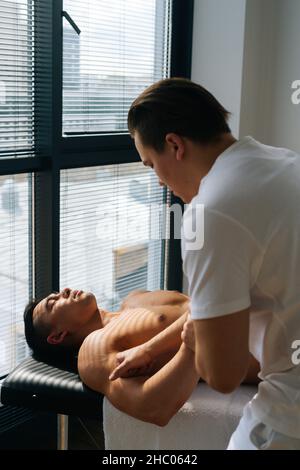 Vertikale Aufnahme des professionellen männlichen Masseurs mit starken Händen massiert Unterarm des muskulösen Athleten Mann nach dem Sport-Training Stockfoto