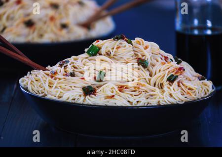 Selektiver Fokus von zwei Schüsseln vegetarischer asiatischer chinesischer Nudeln auf einem schwarzen rustikalen Holztisch mit verschwommenem Vorder- und Hintergrund. Stockfoto