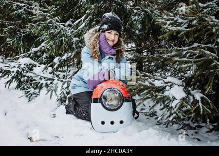 Junge Frau gehen mit Katze in Pet Carrier Rucksack im Winter Park, Wald. Bubble Backpack Carrier für Katzen, Tierreisen, Wandern, Wandern und Outdoor Stockfoto