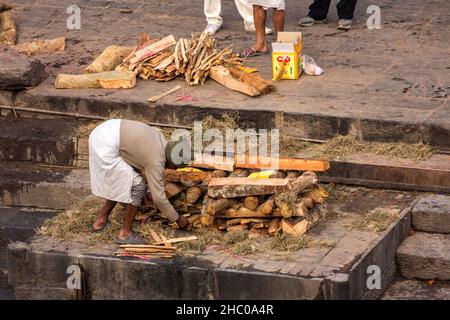 Ein Arbeiter stapelt das Holz für einen Scheiterhaufen in einem Ghat am Bagmati-Fluss, dem Pashupatinath-Tempelkomplex, Kathmandu, Nepal. Stockfoto