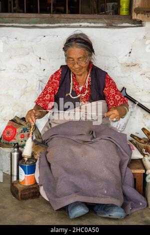 Eine ältere tibetische Flüchtlingsfrau spinnt Wolle per Hand in Garn, um Teppiche in einer Flüchtlingssiedlung in Pokhara, Nepal, zu machen. Stockfoto