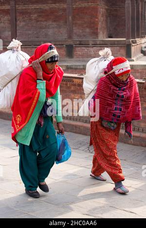 Zwei nepalesische Frauen tragen in Kathmandu, Nepal, schwere Lasten mit einem Bauch- oder Kopfgurt auf ihrem Rücken. Stockfoto