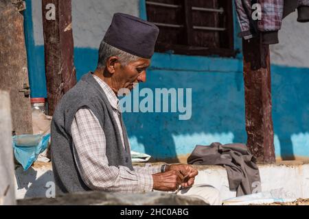 Ein älterer Nepalesischer Mann mit schwarzer Topi-Mütze sitzt vor seinem Haus im Himalaya-Vorgebirgsdorf Dhampus, Nepal. Stockfoto