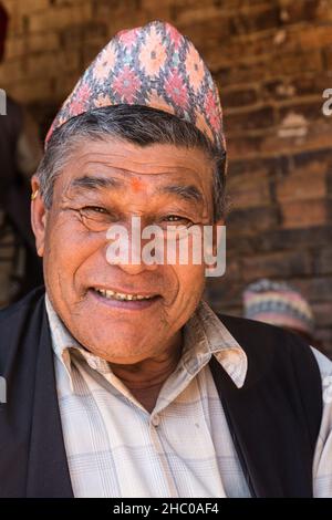 In der mittelalterlichen Stadt Bhaktapur in Nepal sitzt ein älterer Nepalesischer Mann mit einer traditionellen Dhaka-Topi-Mütze im Schatten. Stockfoto