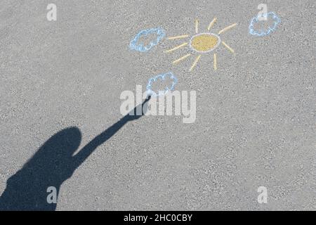 Eine Kinderzeichnung und der Schatten des Kindes auf dem Asphalt. Bunte Zeichnung auf der Asphaltstraße. Blick von oben. Stockfoto