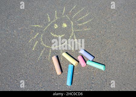 Bunte Zeichnung der Sonne, auf der Asphaltstraße. Mehrfarbige Buntstifte auf Asphalt aus nächster Nähe. Stockfoto