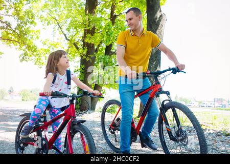 Glücklicher Vater mit Tochter auf Rädern im Park an einem sonnigen Tag. Stockfoto