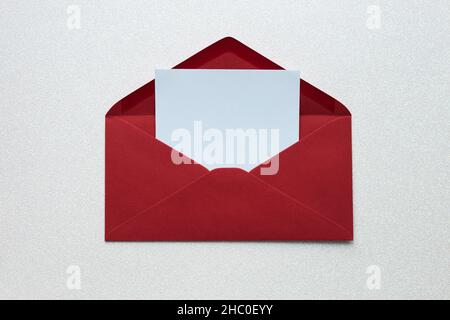 Offener roter Umschlag mit leerem Schreibpapier auf silbrig glänzendem Hintergrund, Platz für Text Stockfoto